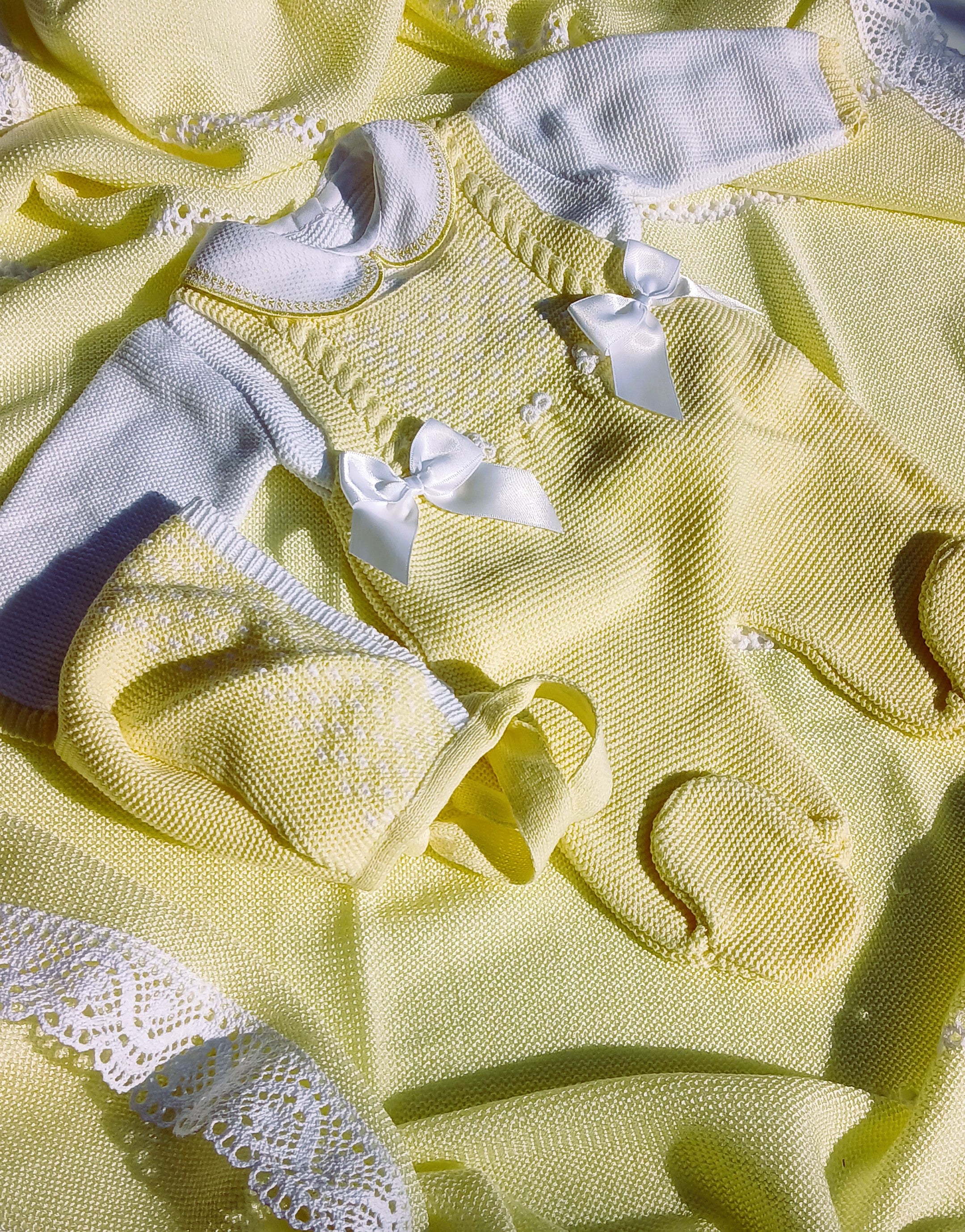 Close-up of a yellow baby outfit with white ribbons and lace details.