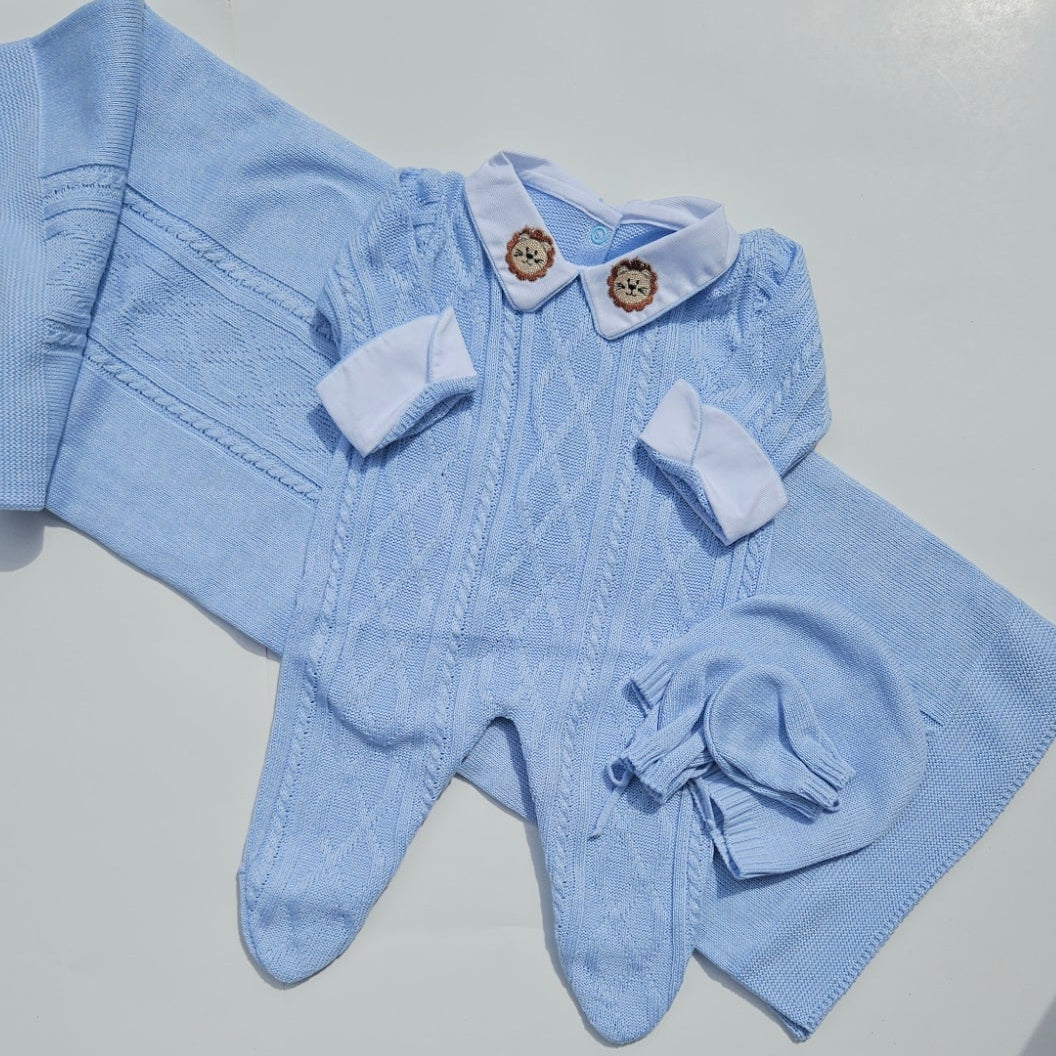 Blue baby outfit on a white surface with a person's feet in sandals in the background.
