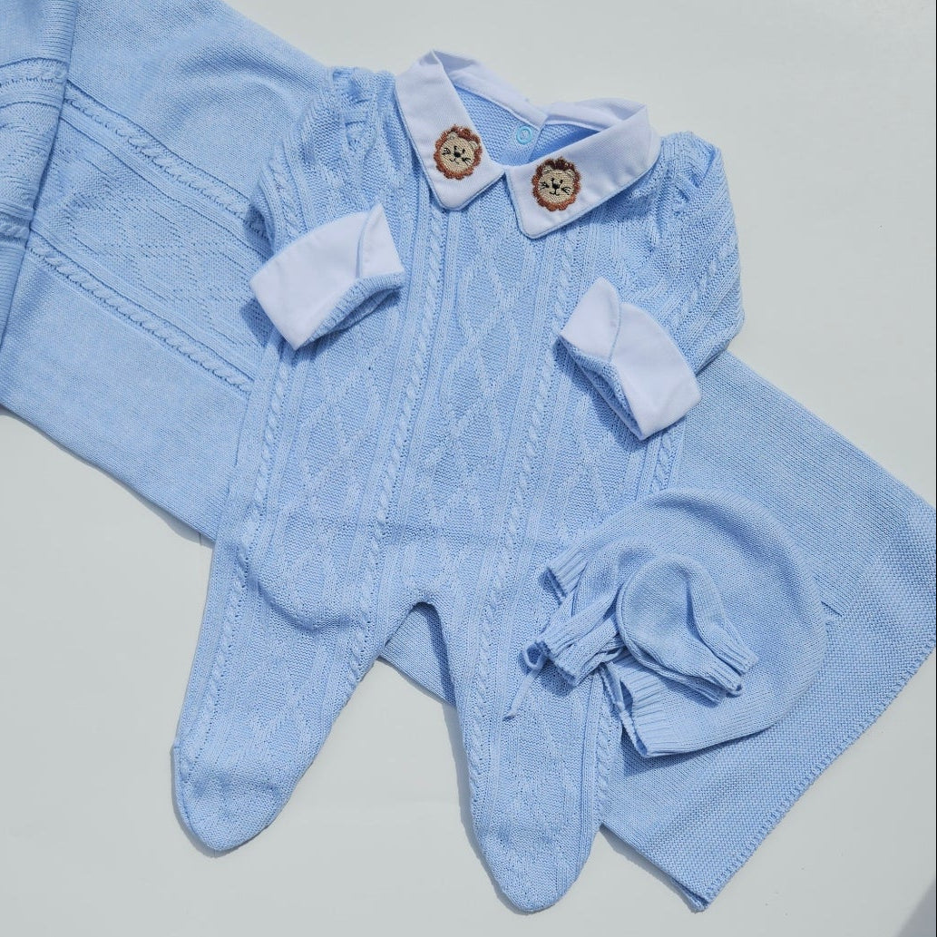 Light blue baby outfit on a white surface with a person's legs in black and white patterned pants in the background.