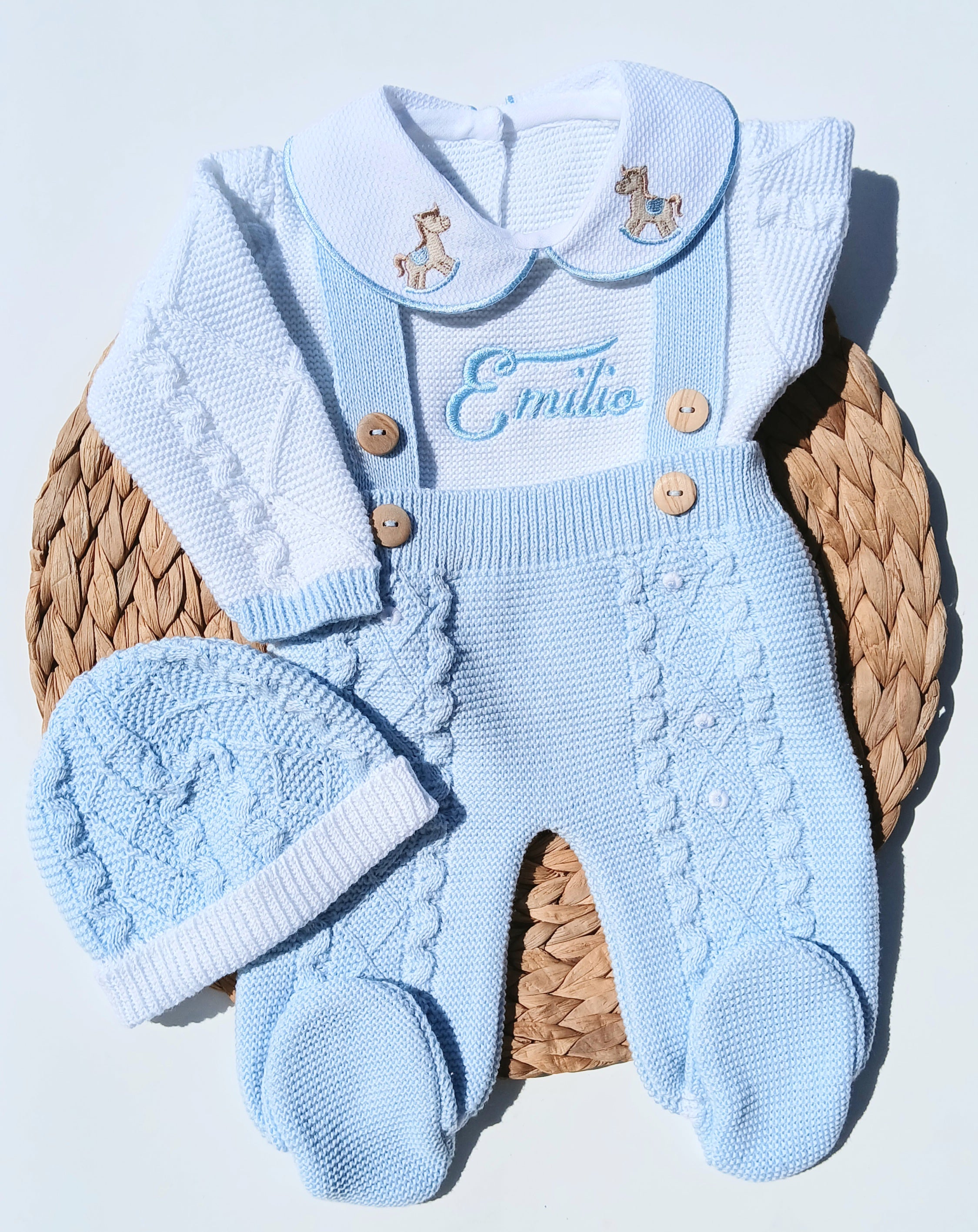Knitted baby outfit with overalls, shirt, and hat on a woven basket