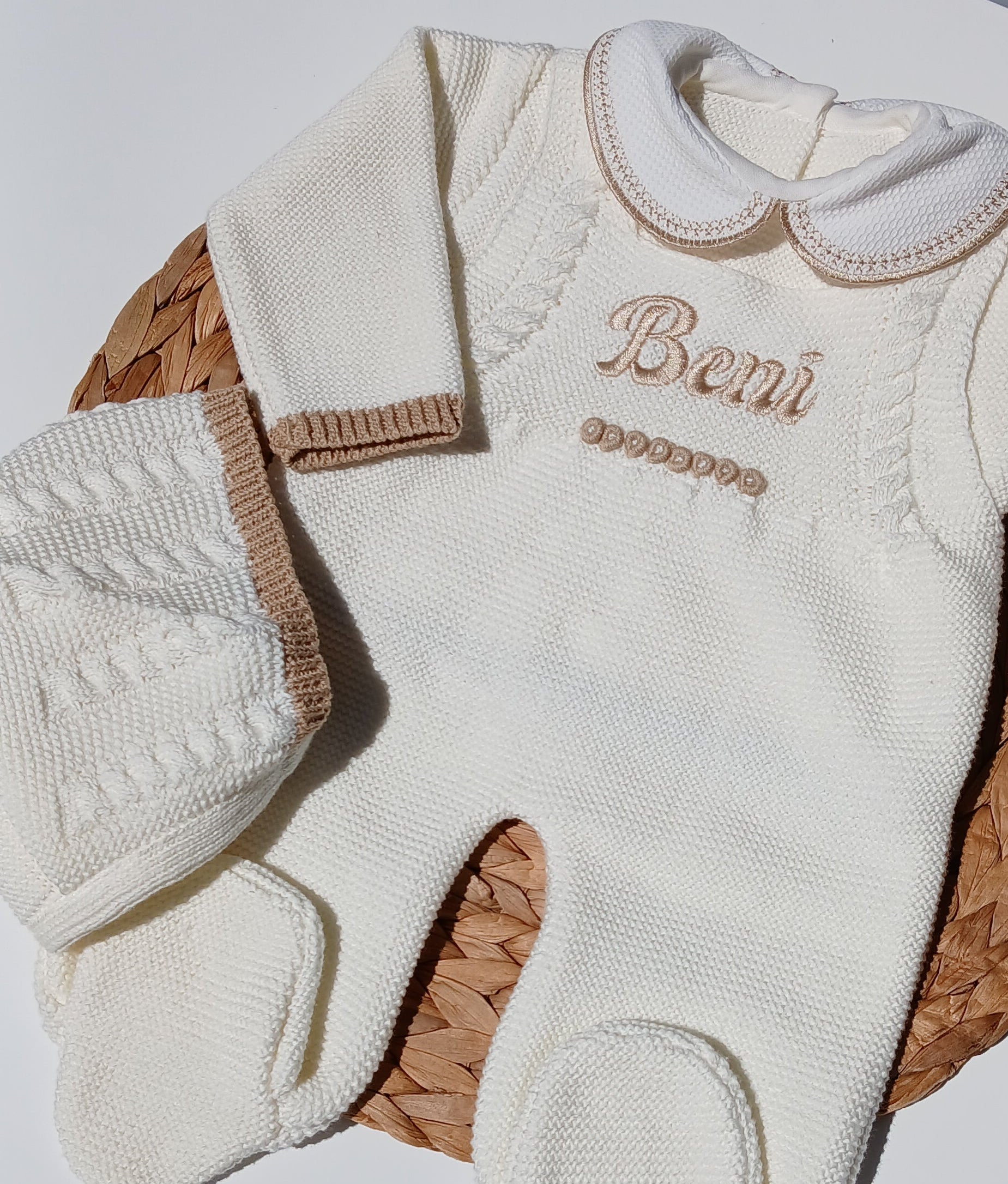 A baby knit mittens set in cream/off-white with tan trim, featuring the brand name 'Beni' embroidered on one mitten, displayed on a woven straw mat over a white surface.