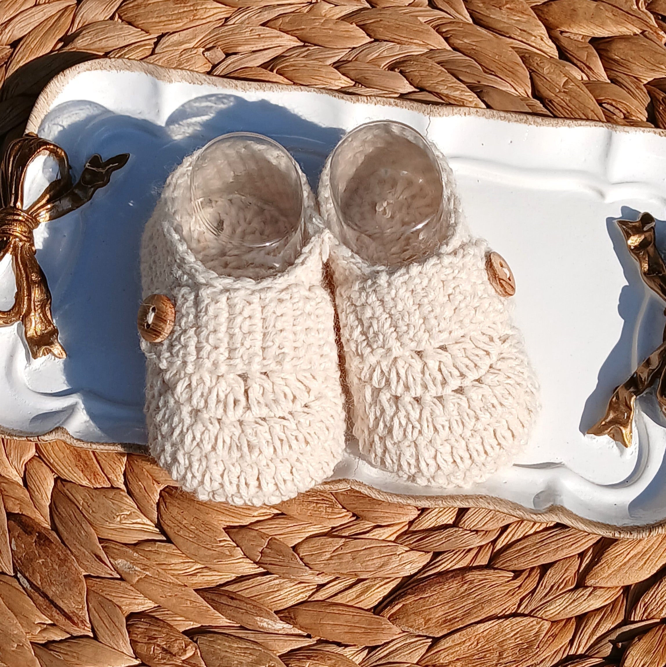 Pair of white slippers on a decorative tray with gold accents, placed on a woven surface.