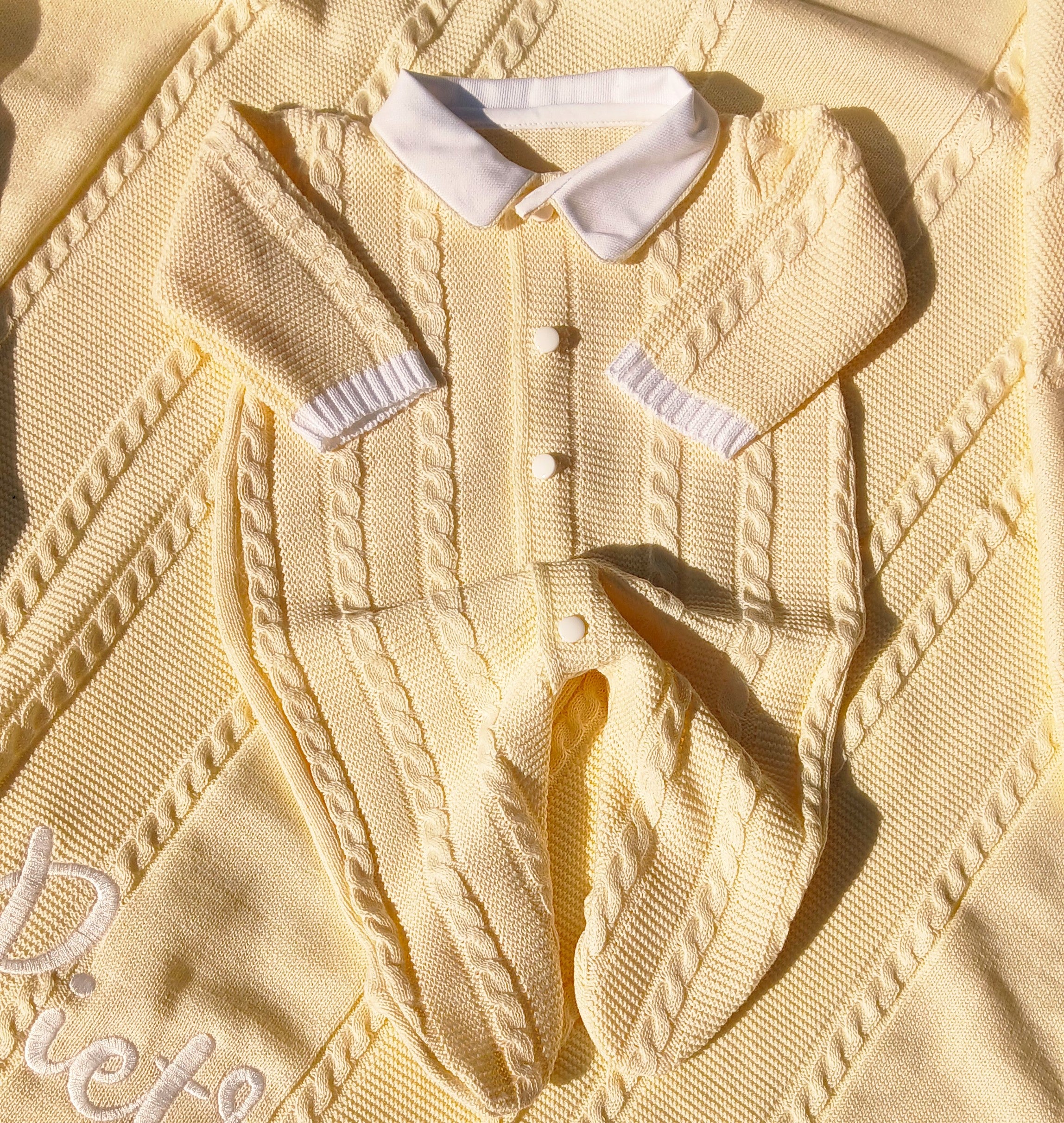 Close-up of a beige knitted cardigan with white buttons and trim on a matching fabric background.