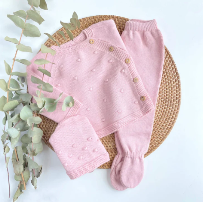 Pink baby outfit with matching hat on a woven mat with green leaves.