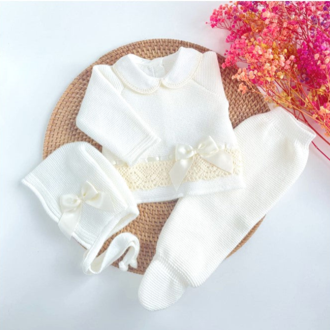 ivory baby outfit with a bow on a woven mat with pink flowers in the background