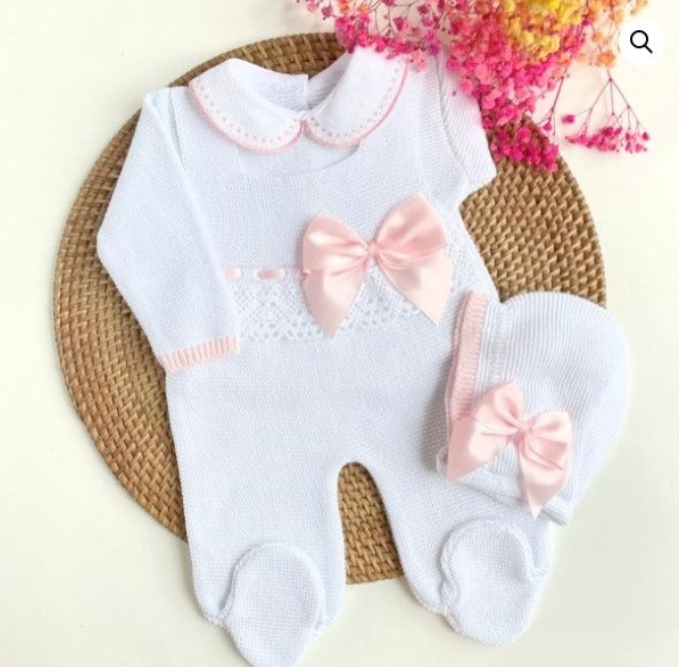 Baby onesie with pink bows on a woven mat, newborn white knit romper