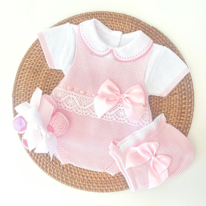 Pink baby outfit with white accents on a woven mat