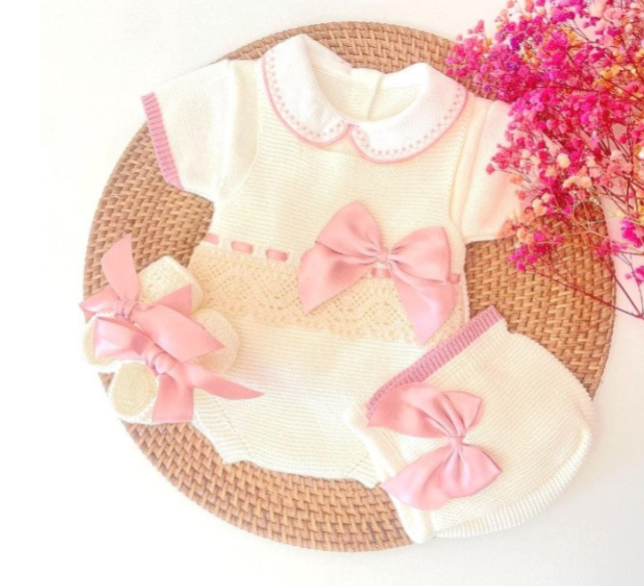 Baby outfit with pink bows on a woven surface