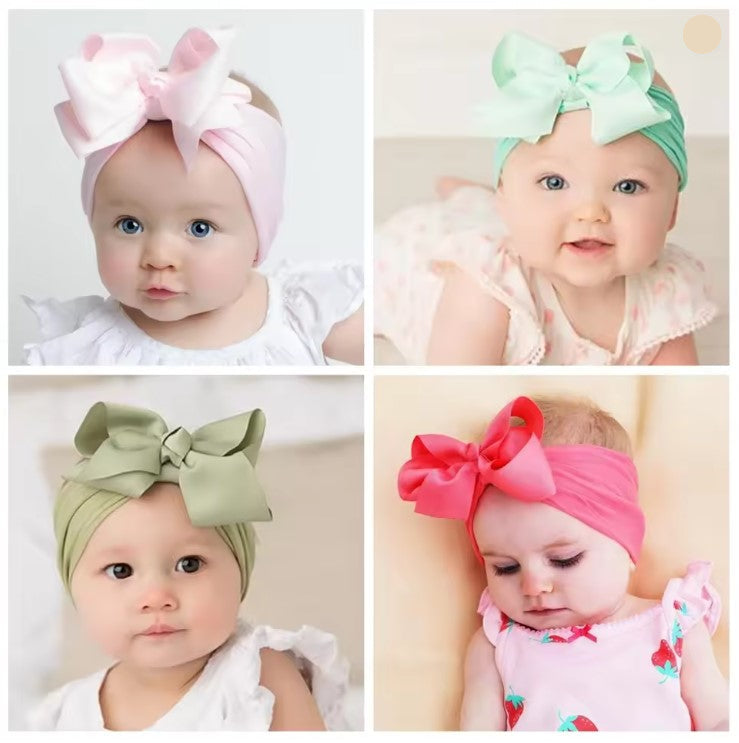 Four baby headbands with large bows in different colors on a plain background.