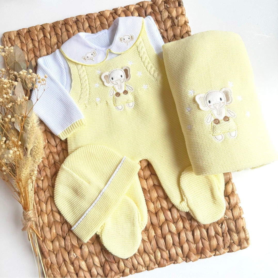 A yellow knitted baby outfit with an elephant design, laid out on a wicker surface, including a cardigan, hat, and a pair of booties.