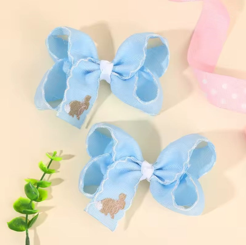 Two blue hair bows with embroidered designs on a beige background. Easter bunny embroidered
