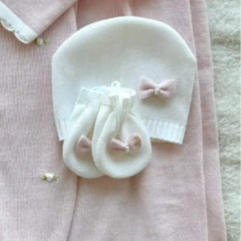 Baby outfit with pink sweater, white hat, and socks on a soft surface