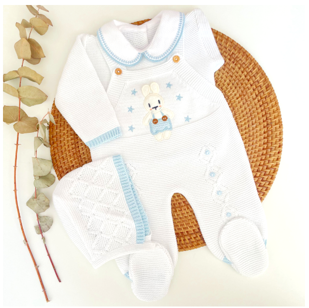 A three-piece knitted baby outfit featuring a white and light blue color scheme with a cute little bunny design, displayed on a wicker mat next to some decorative elements. for newborn coming home from hospital
