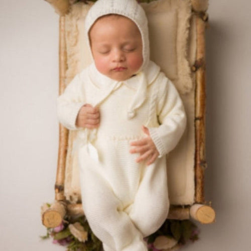 Newborn baby in a white outfit lying on a wooden crib with flowers around. , newborn knit going home outfit, newborn baby girl coming home knit outfit