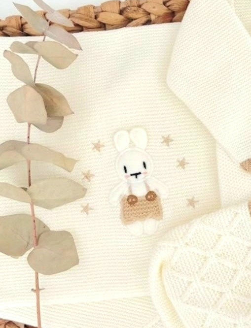 Baby outfit with white sweater, pants, and hat featuring animal designs on a woven basket background.