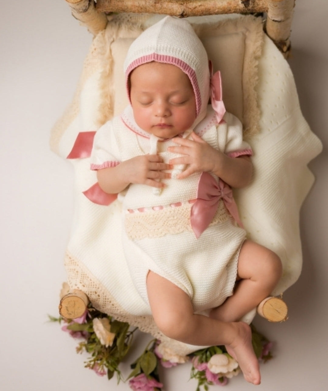 Newborn baby in a wooden crib with floral decorations baby knit ivory outfit