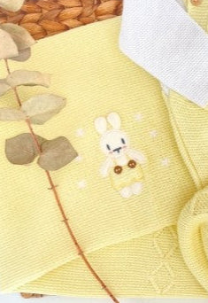 Yellow baby sweater set with bunny designs on a woven tray.