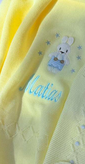 Yellow baby outfit with embroidered name and bunny design on a white background