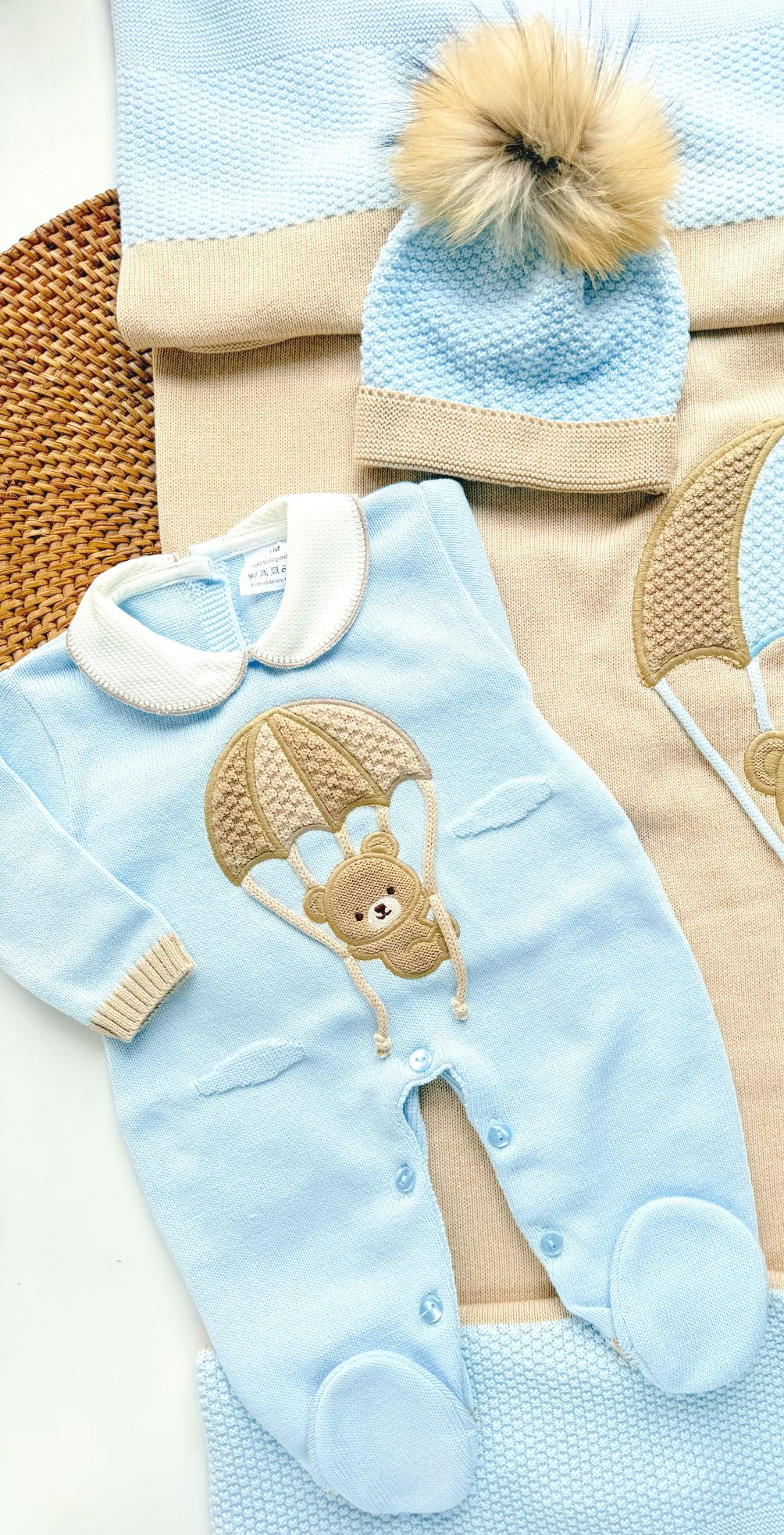 Baby outfit with blue romper, hat, and blanket featuring teddy bear designs on a textured surface.