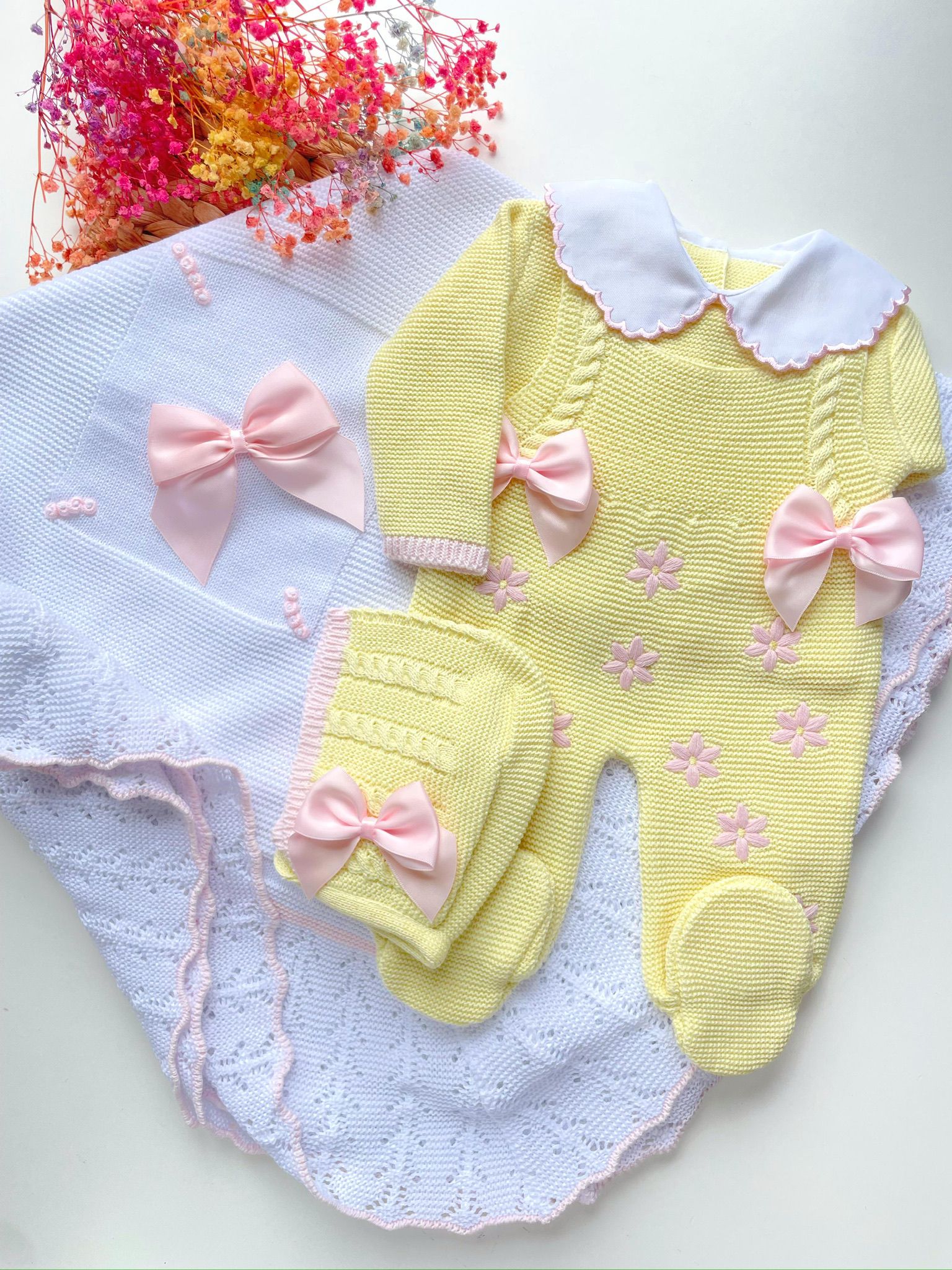 Yellow baby romper with pink bows on a white blanket