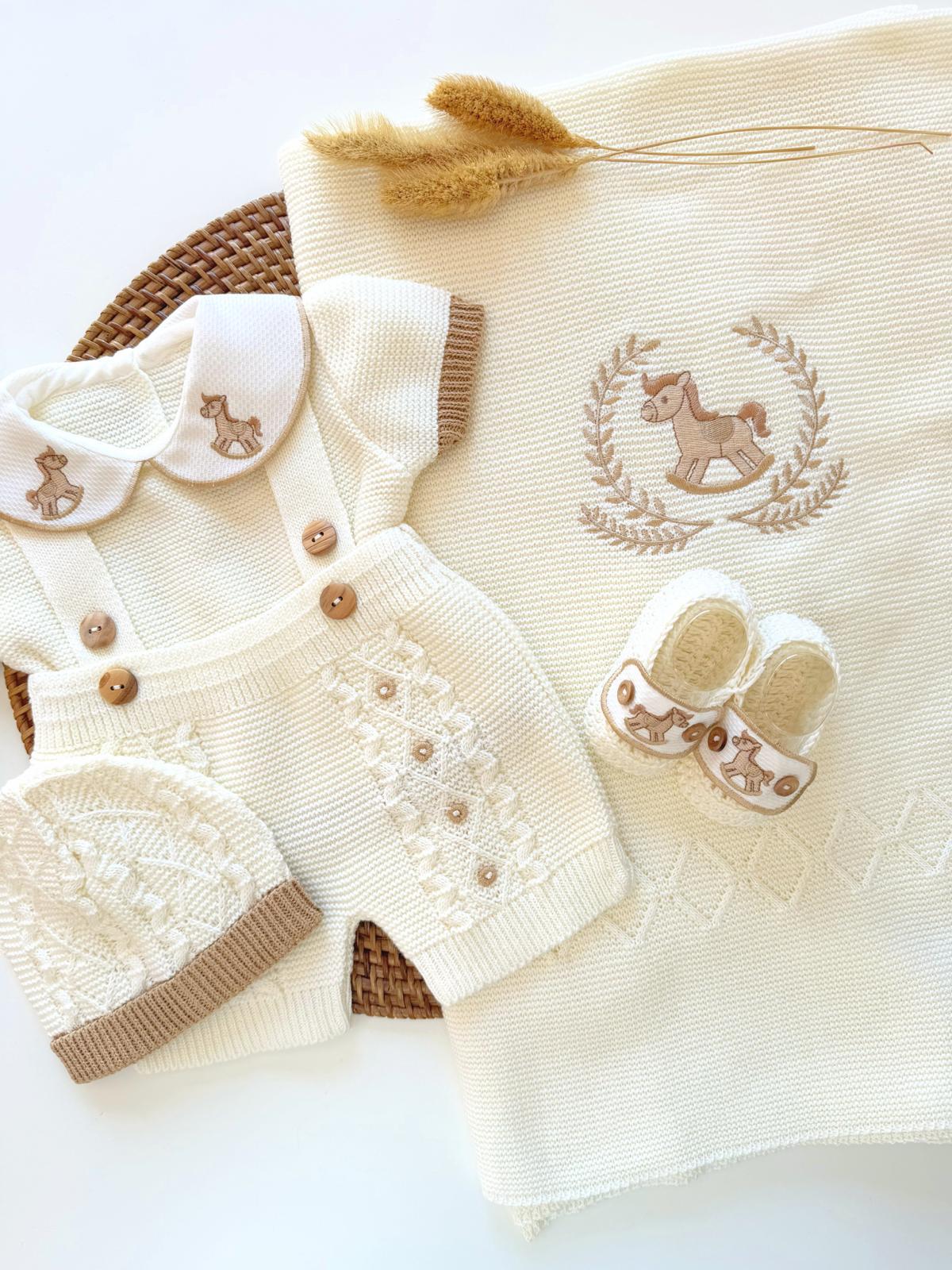 Baby outfit with white romper and hat, beige blanket with embroidered design, on a light background