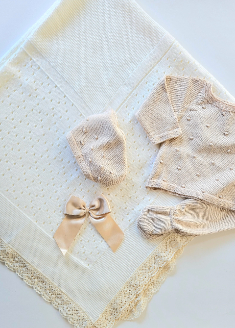Baby outfit with knitted romper, booties, and headband on a textured white surface