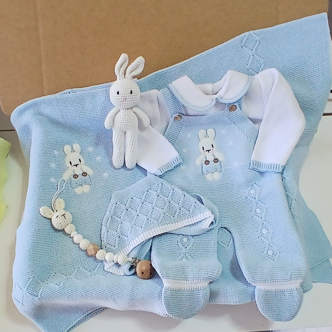 Baby shower gift set with blue blanket, white booties, and other items on a table.