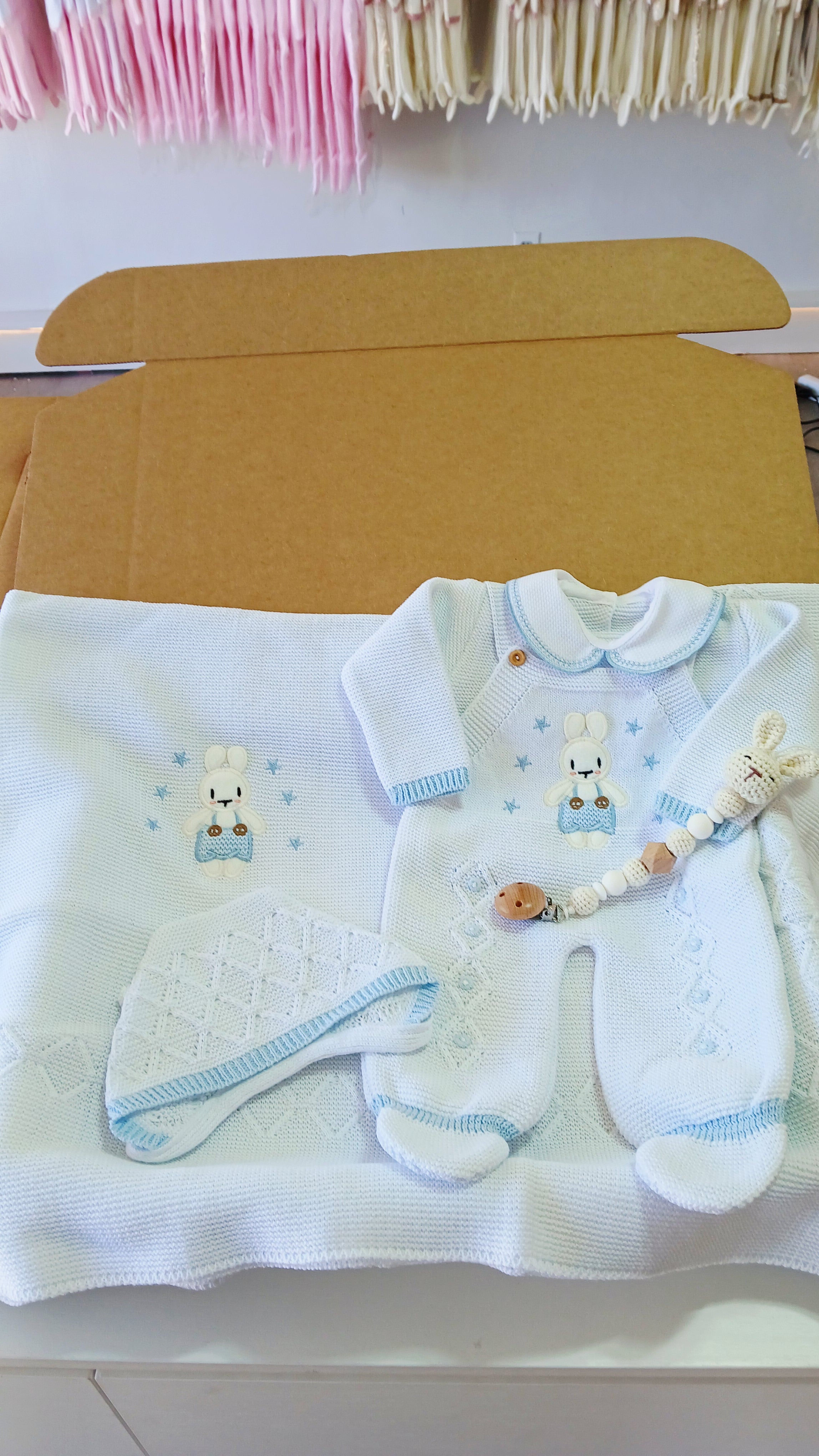 Baby clothing and accessories on a white surface with a cardboard box.