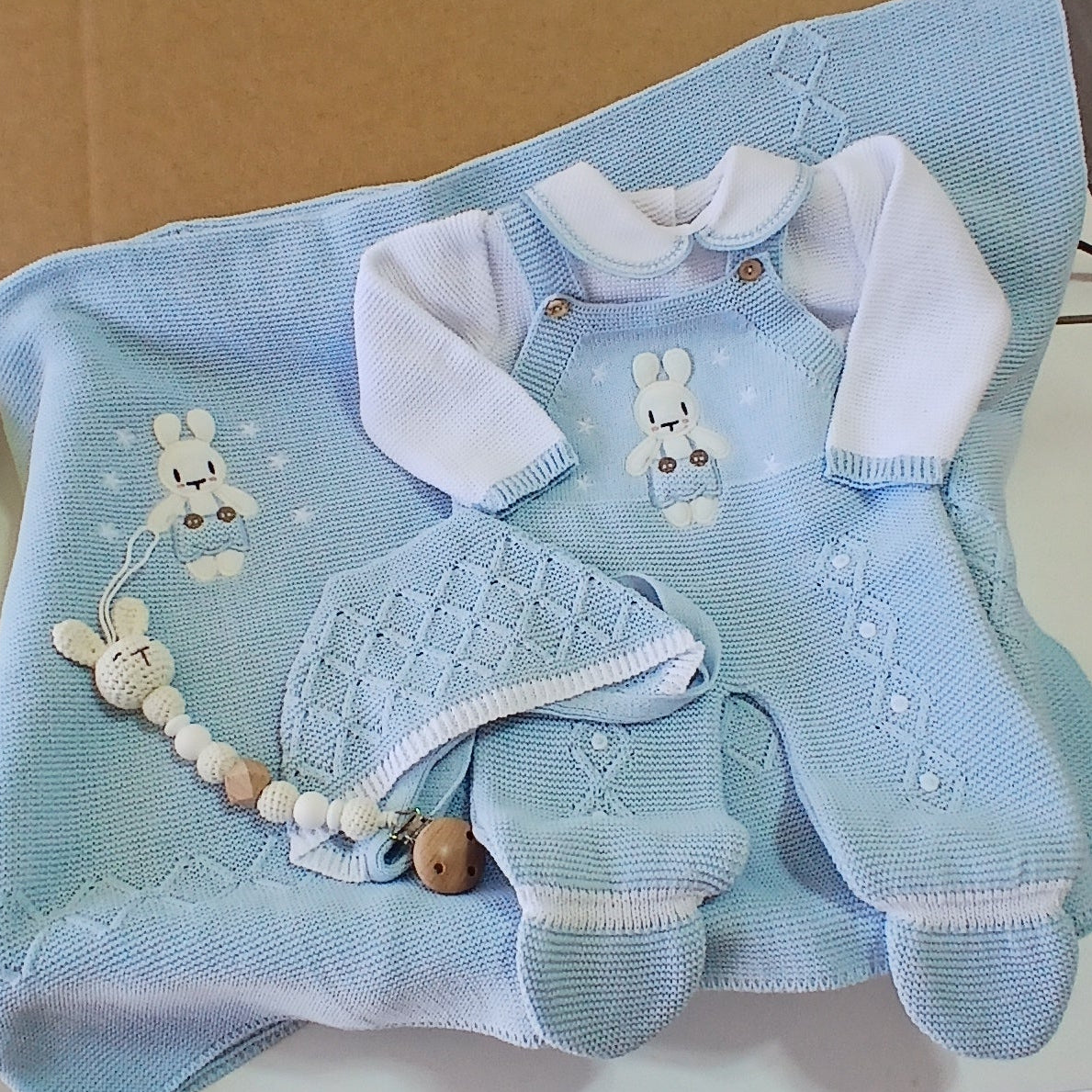 Baby outfit with blue romper, white pants, and headband on a cardboard box.