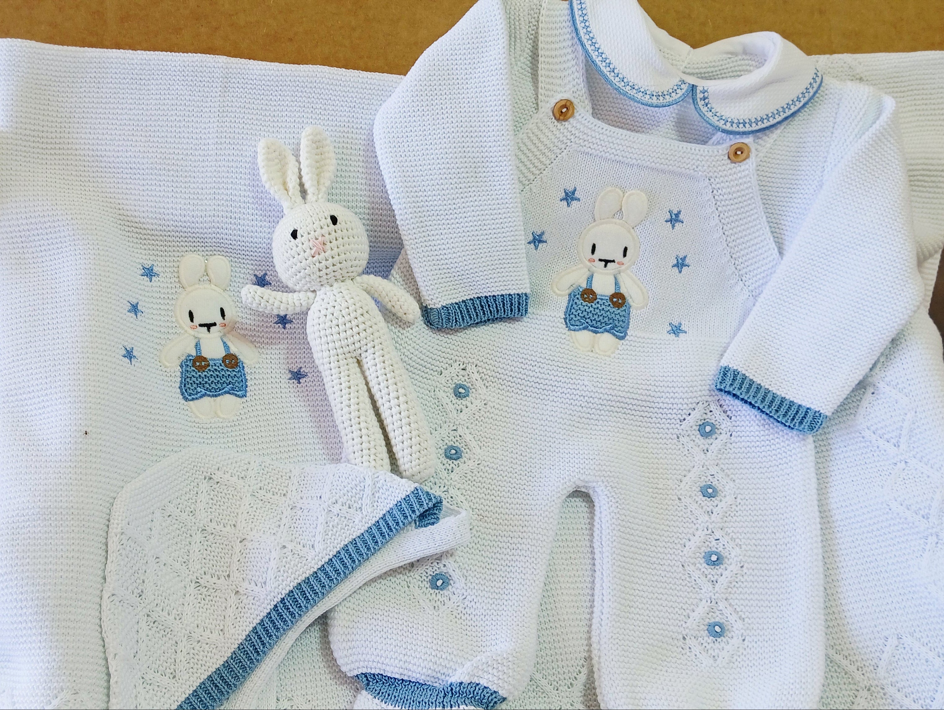 Baby clothing set with white onesie, hat, and blanket on a brown surface