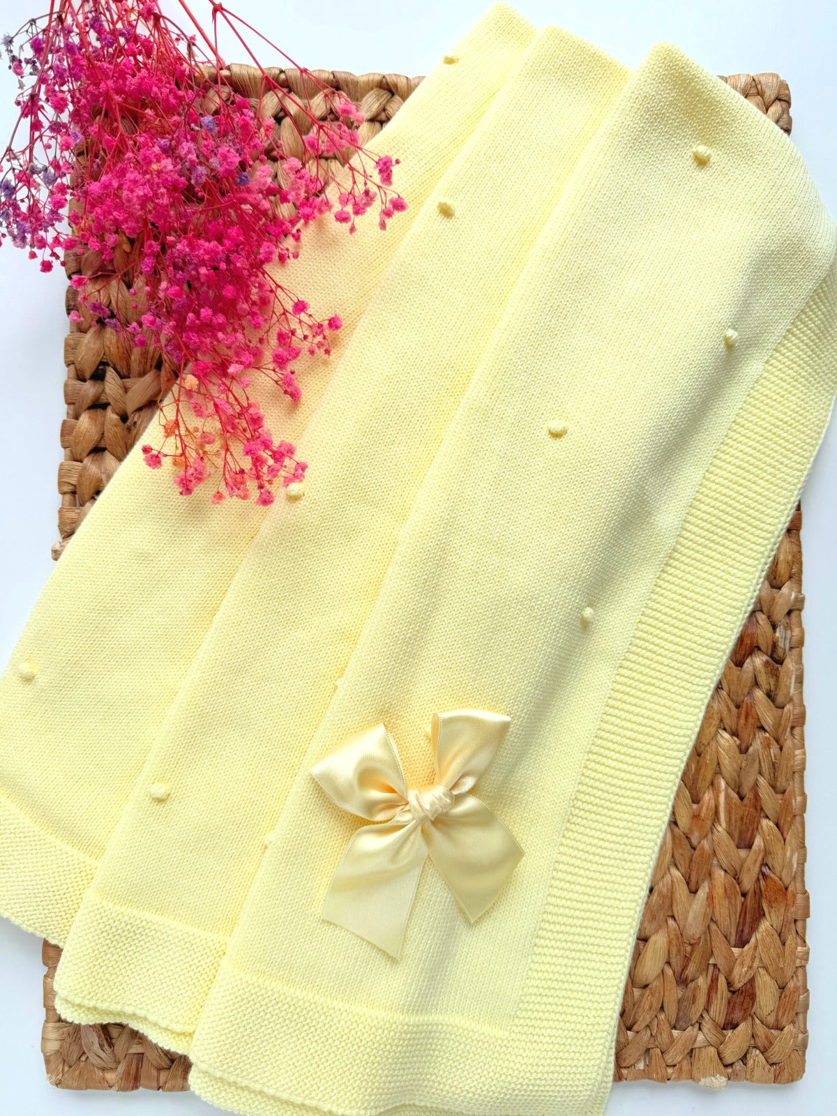 Set of yellow baby blankets with a bow on a woven mat with pink flowers.
