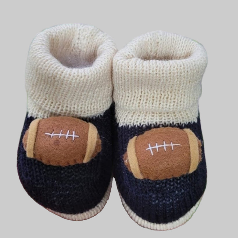 Knitted baby booties with football design held in front of green foliage