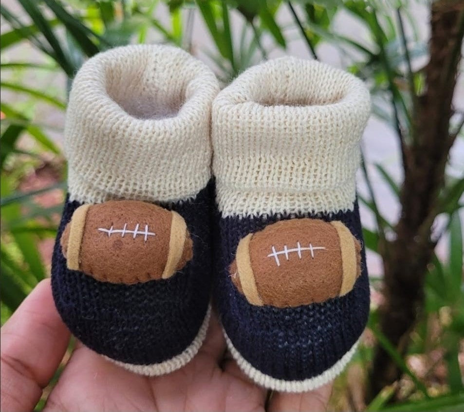Knitted baby booties with football design held in a hand against a blurred green background