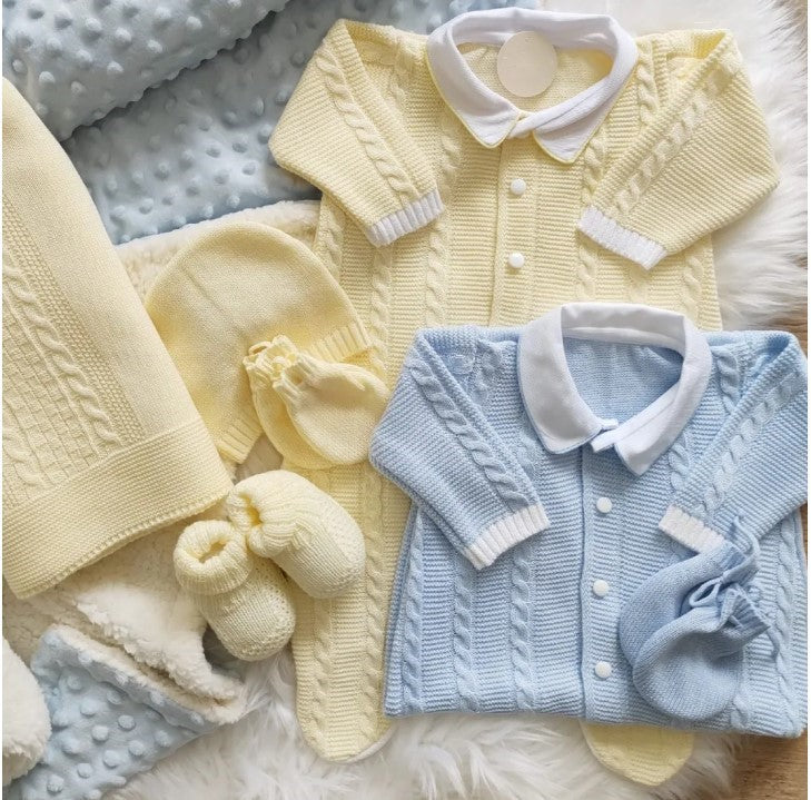 Set of baby knitted cardigans and accessories in yellow and blue on a textured surface.