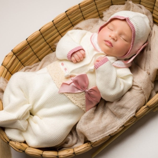 Newborn baby in a basket wearing a white outfit with pink accents and a matching hat.