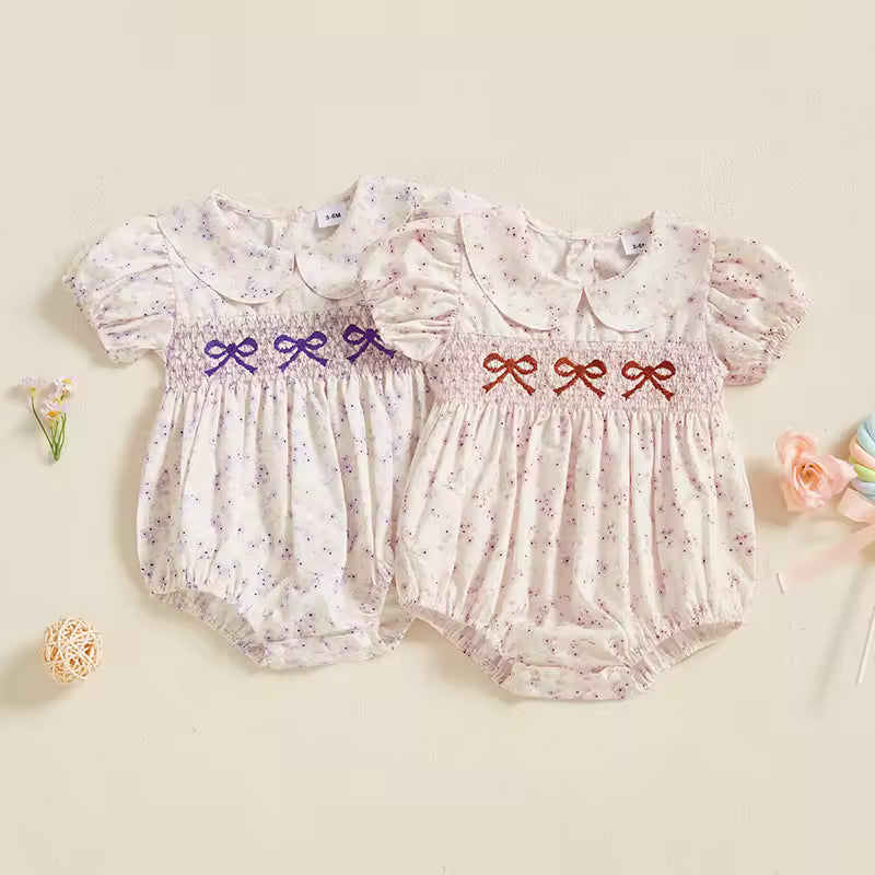 Two baby rompers with floral patterns and embroidered bows on a beige background