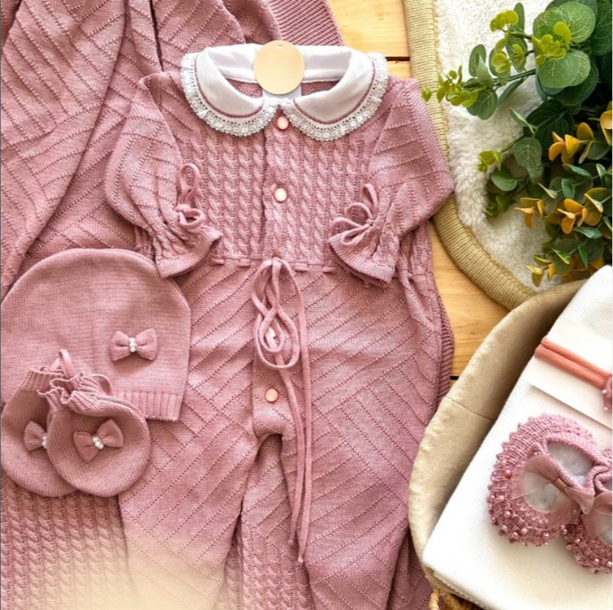 Pink baby outfit with matching hat and bag on a textured surface.