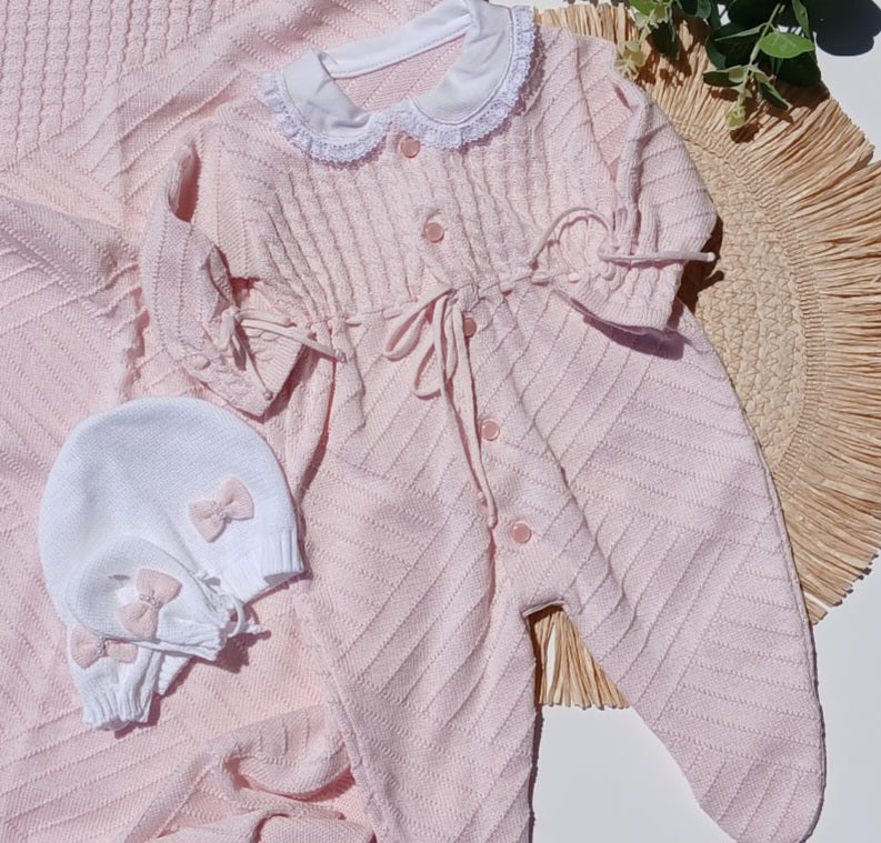 Pink baby outfit with white hat on a textured surface