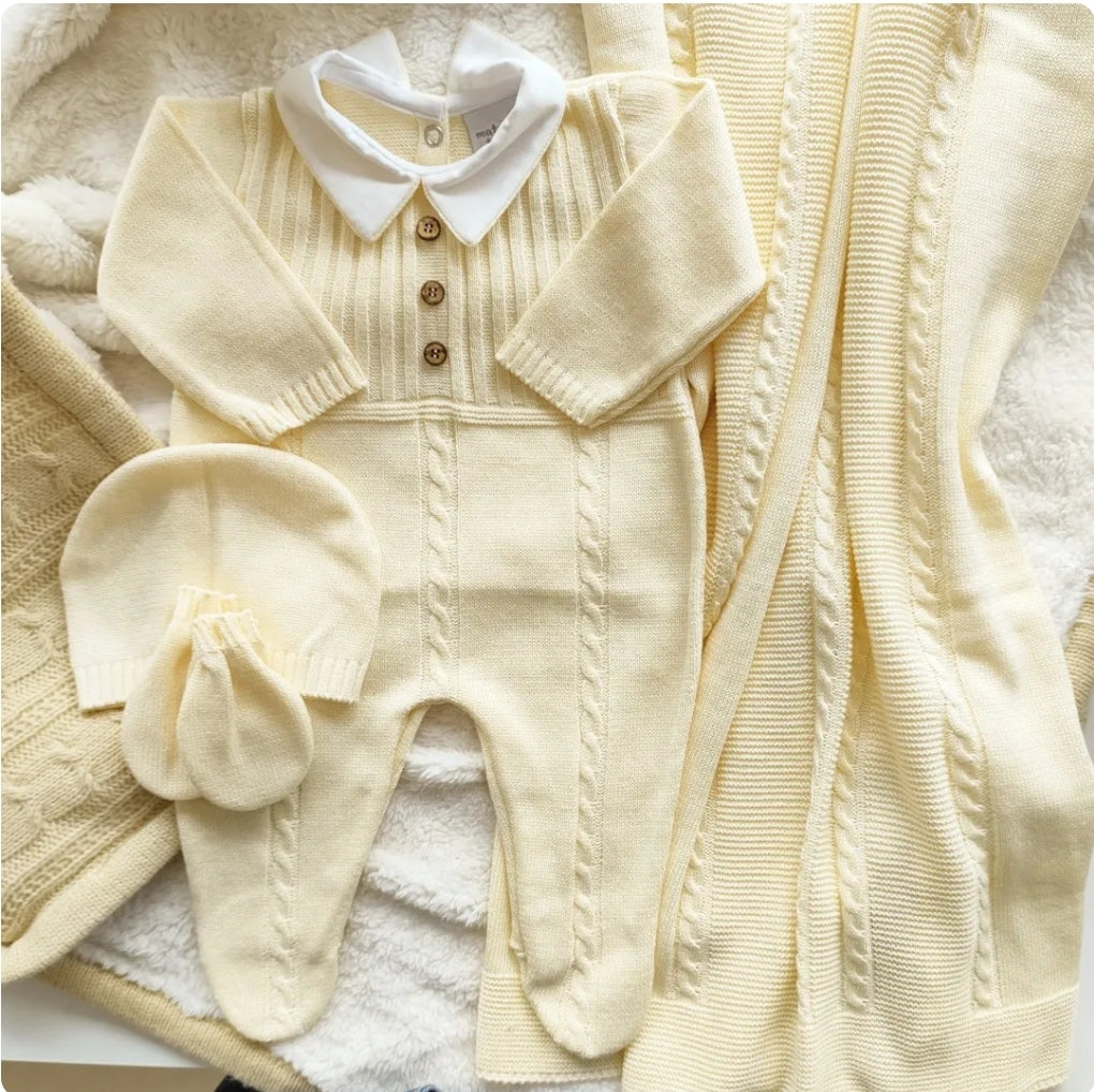 Cream-colored baby outfit with matching hat and booties on a textured surface