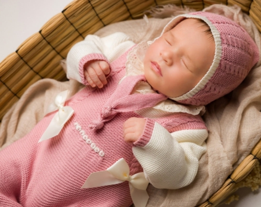 Newborn baby in a pink outfit with a bow, lying in a woven basket.