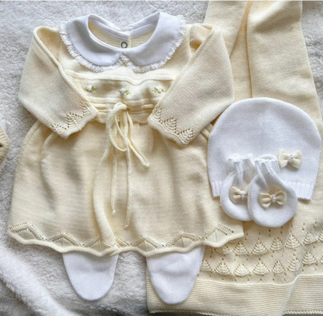 Baby outfit set with dress, cardigan, booties, and hat on a textured surface, newborn yellow little dress