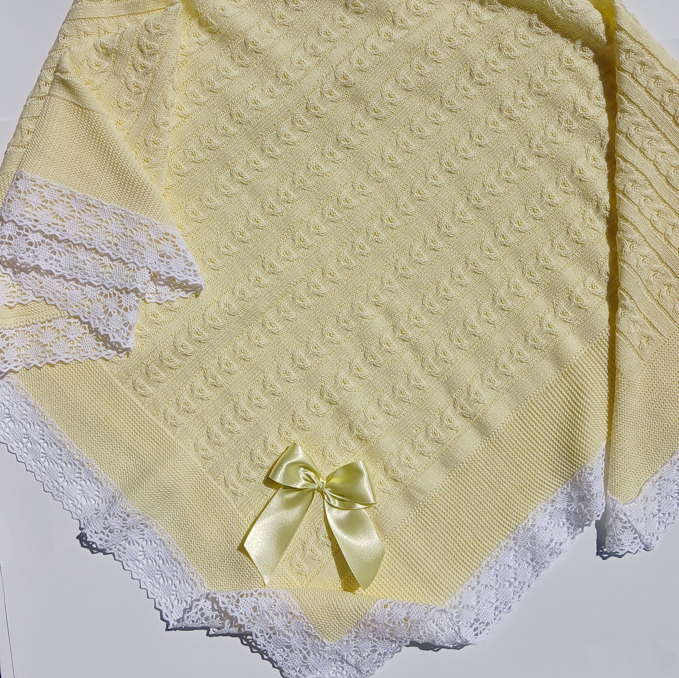 Yellow textured blanket with a bow and lace trim on a white background