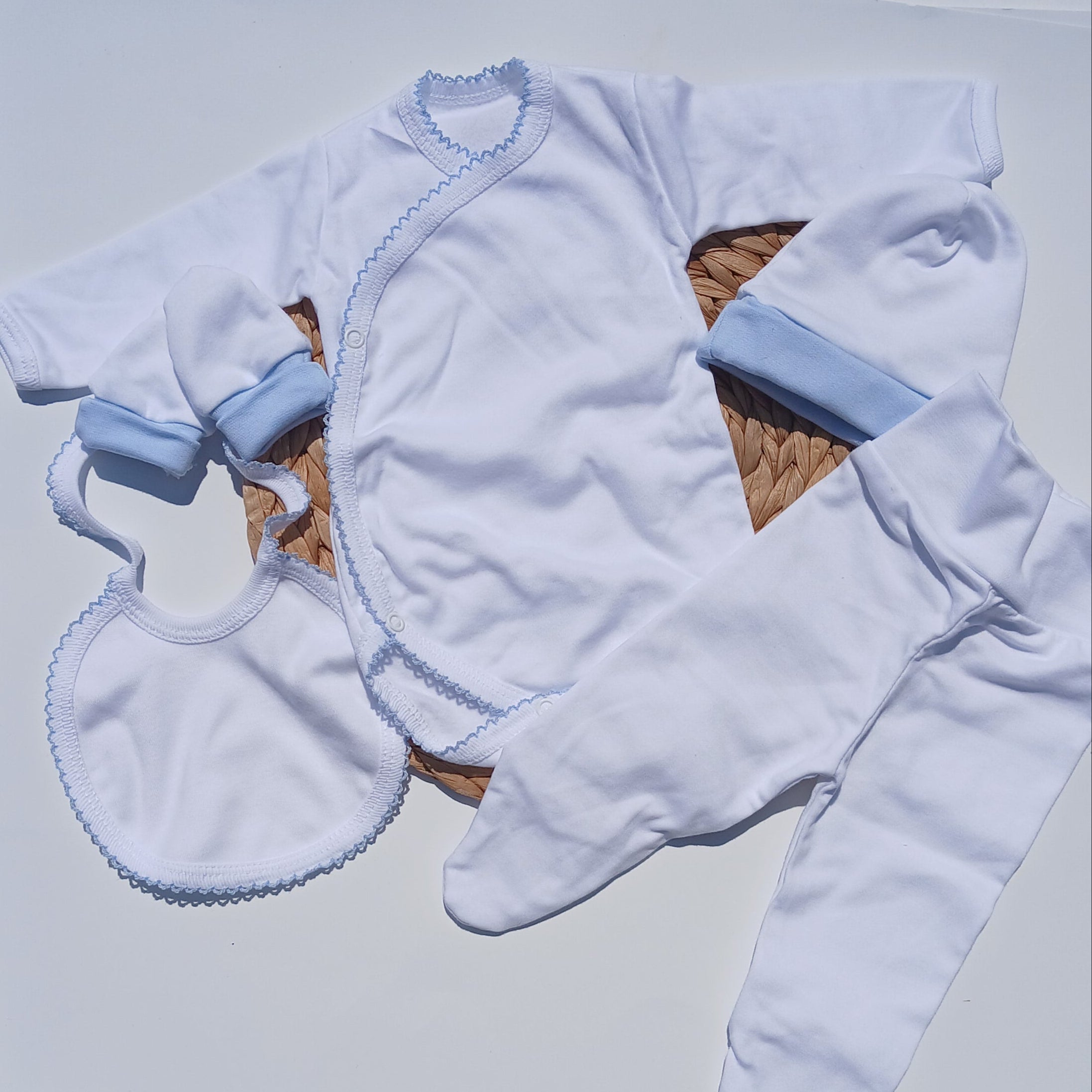 Baby outfit with white bodysuit, hat, and bib on a white surface.