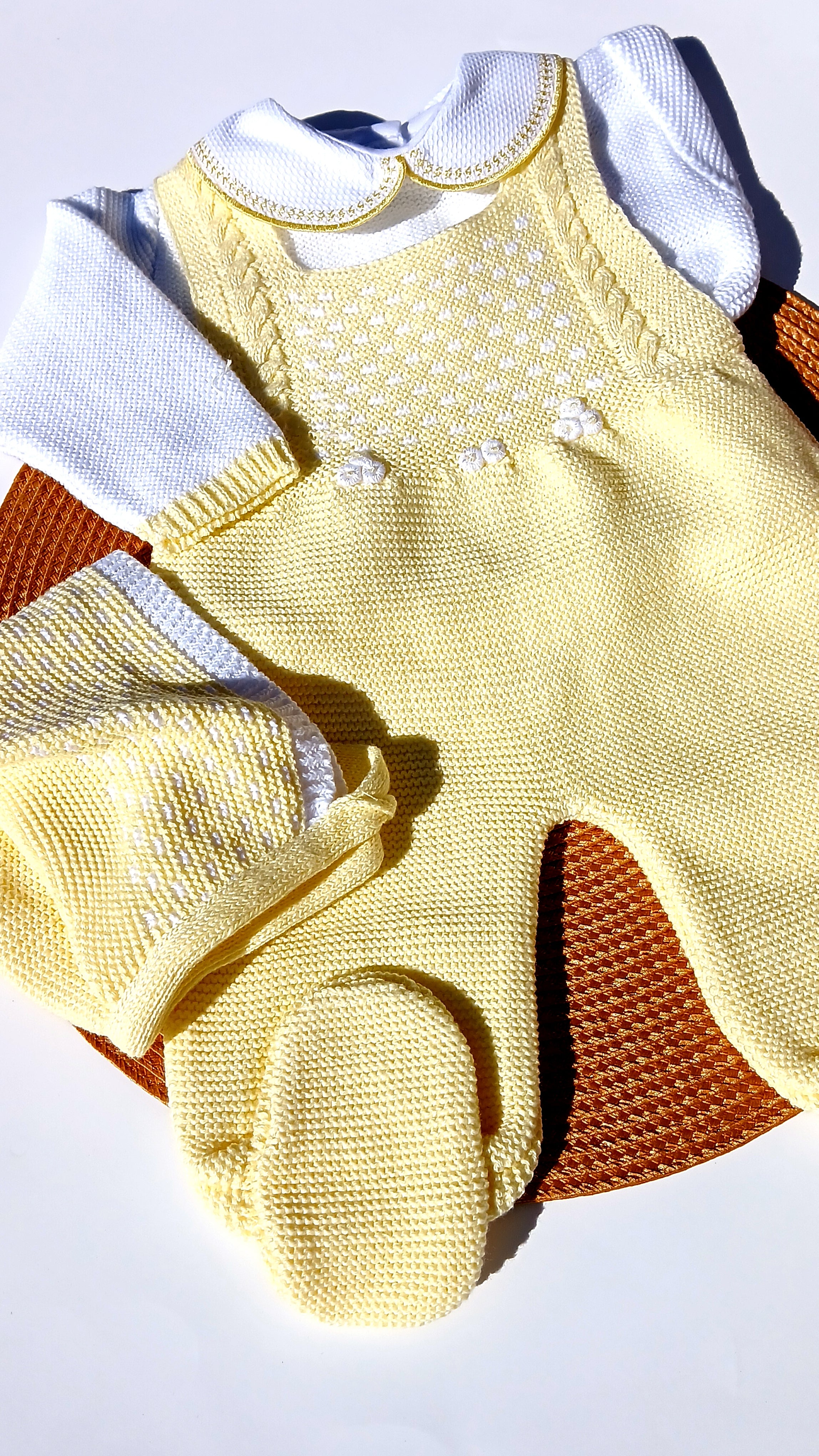 knit Yellow baby outfit with white pants and brown accents on a light gray background