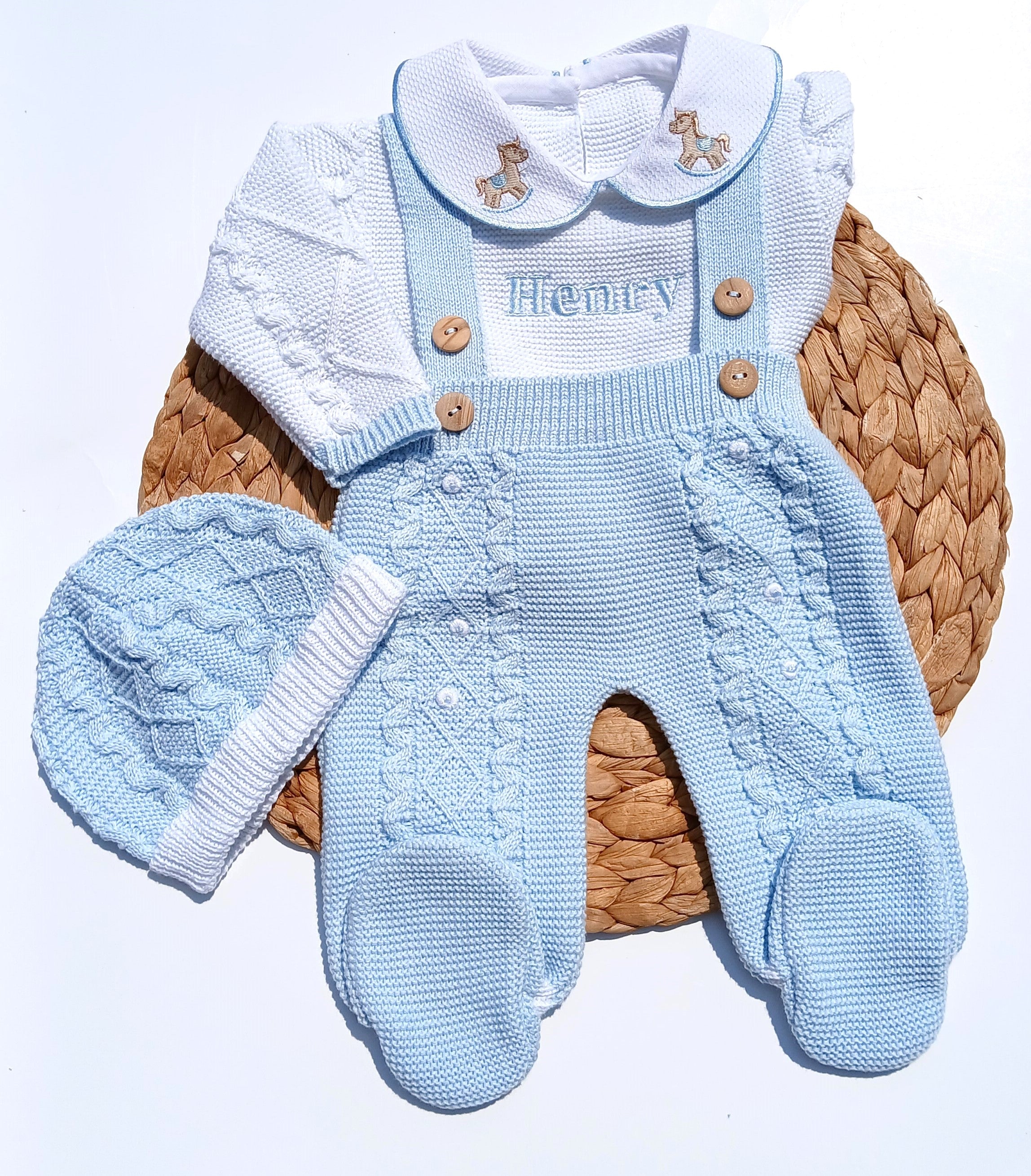 Blue knitted baby outfit with overalls and hat on a woven basket horse