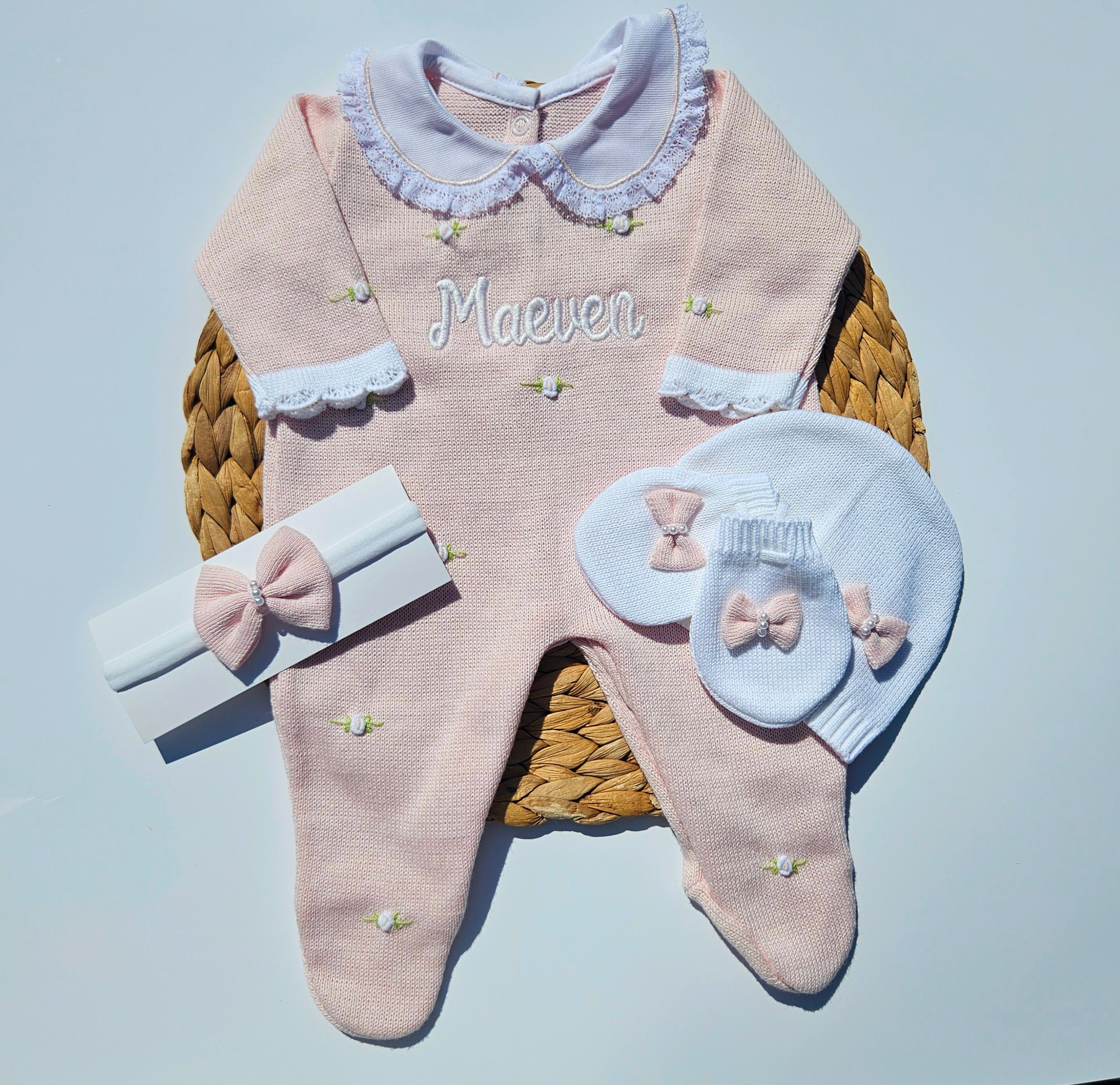 Baby knit flower outfit set with pink romper, white hat and mittens, and headband on a light blue background