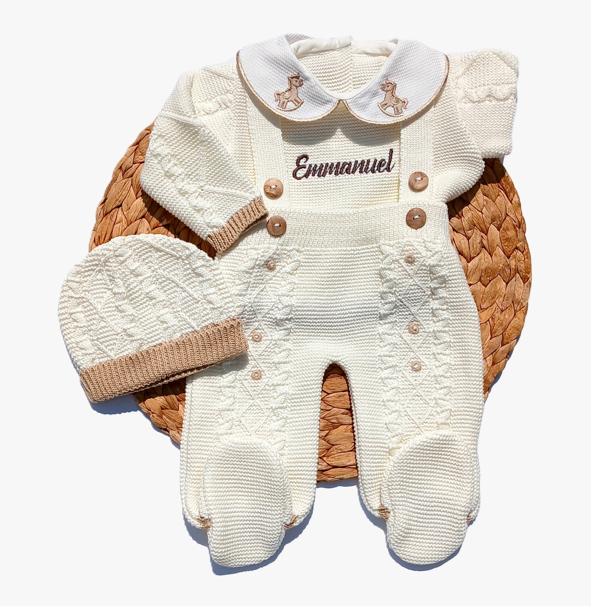 Rocking horse baby outfit White baby outfit with brown accents and 'Emmanuel' embroidery on a woven basket.
