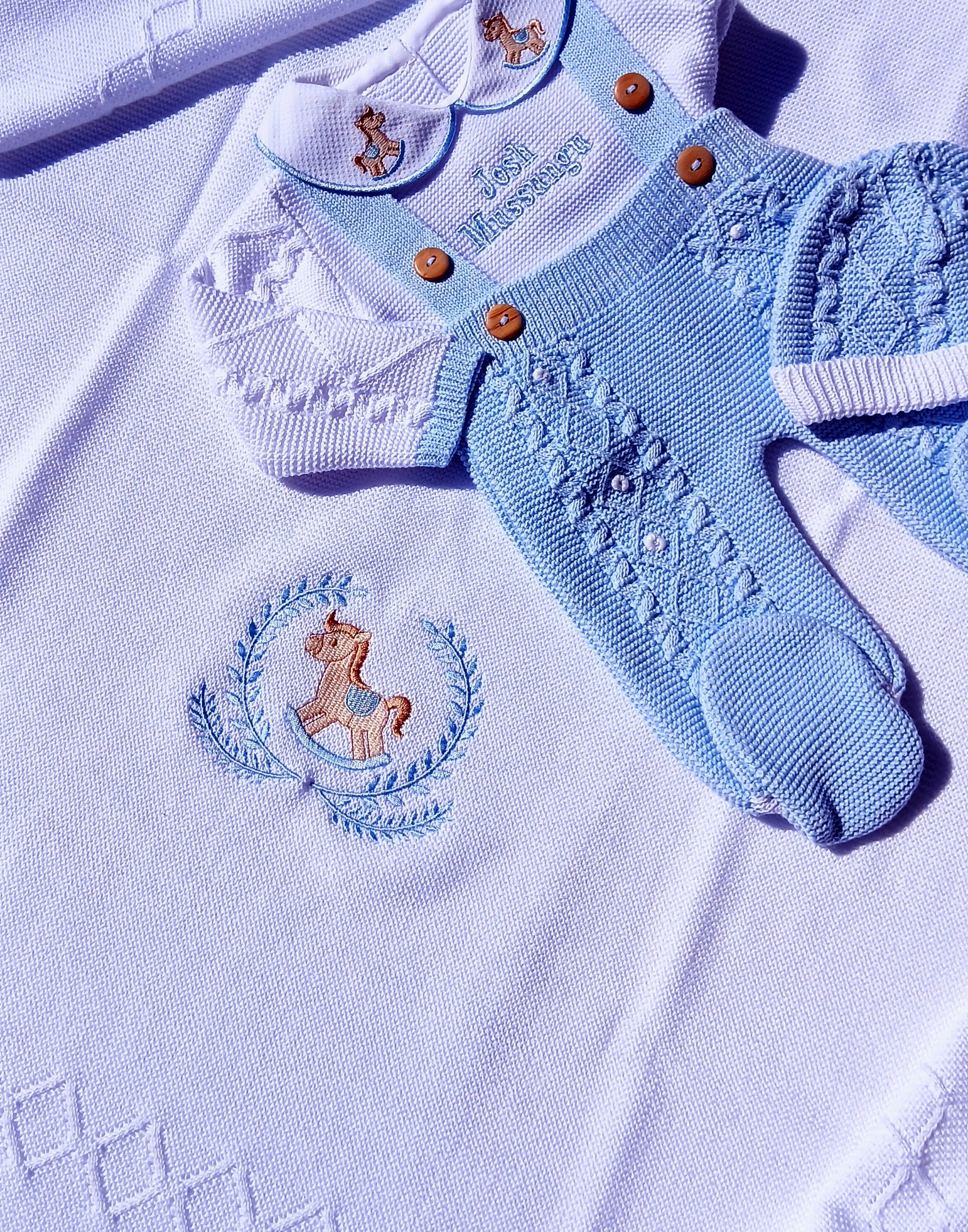 Baby blue knitted outfit with embroidered designs on a white fabric background