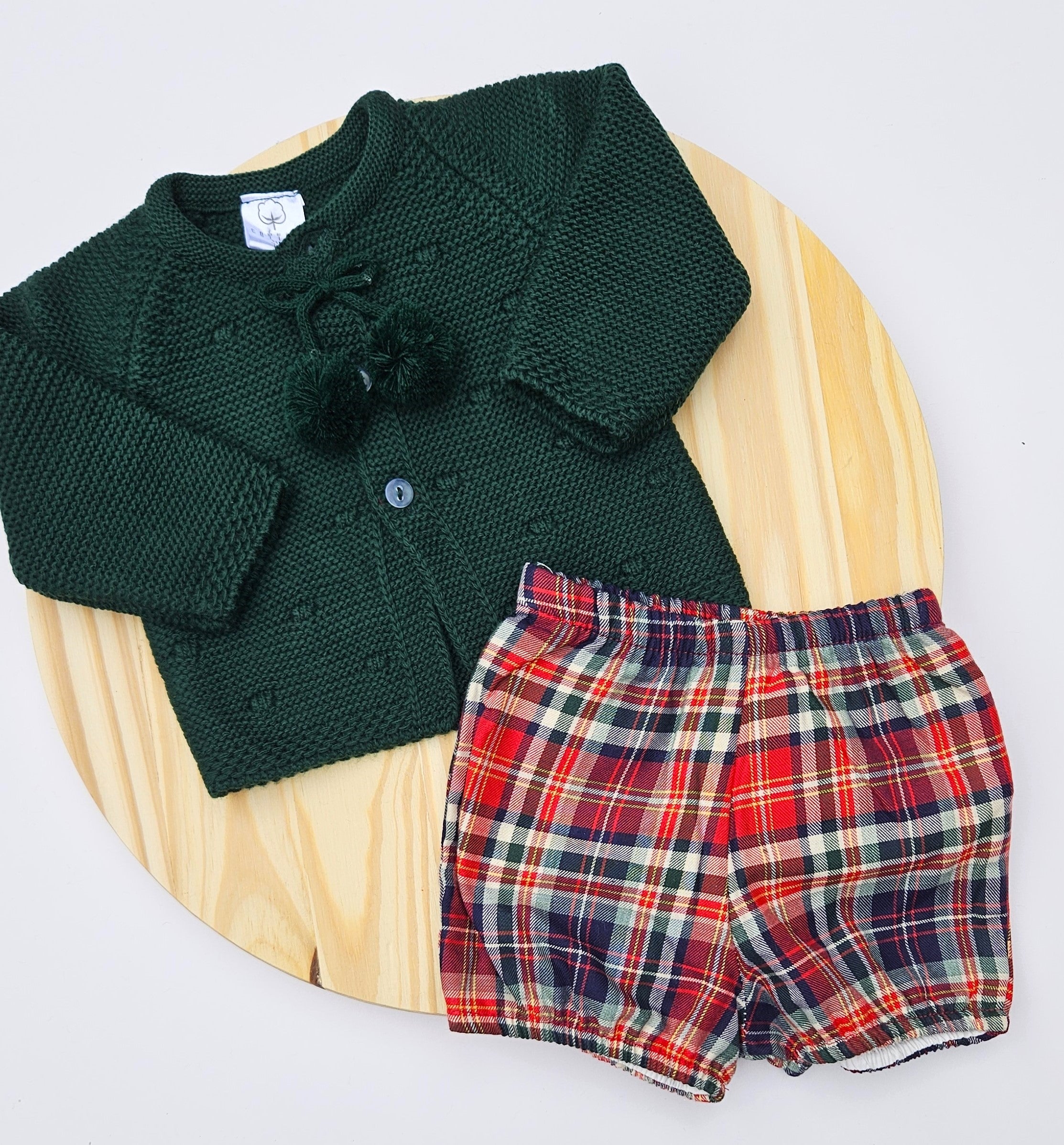 Green knitted cardigan and plaid shorts on a wooden surface Celebrate the season in style with this charming boys Christmas outfit featuring a cozy knitted sweater paired with a coordinating plaid bloomers. This two-piece set keeps your little one comfortable and festive all day long. The classic color options make it perfect for holiday photos. Easy to dress and undress.