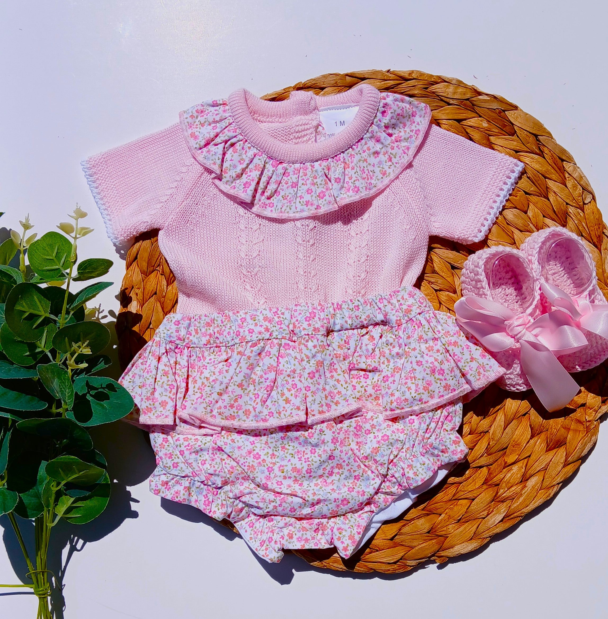 Pink baby outfit with floral details on a woven mat